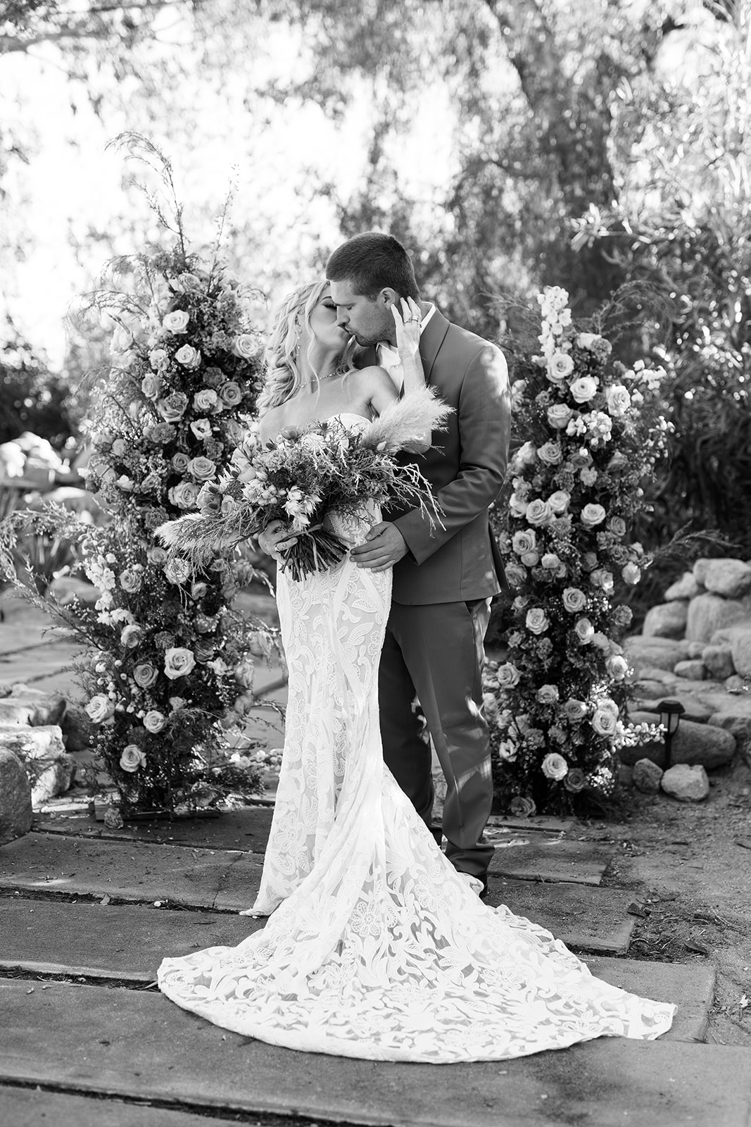 black and white wedding photo with bride kissing groom while standing at wedding flower arbor for elopement ceremony, elopement photographer in austin