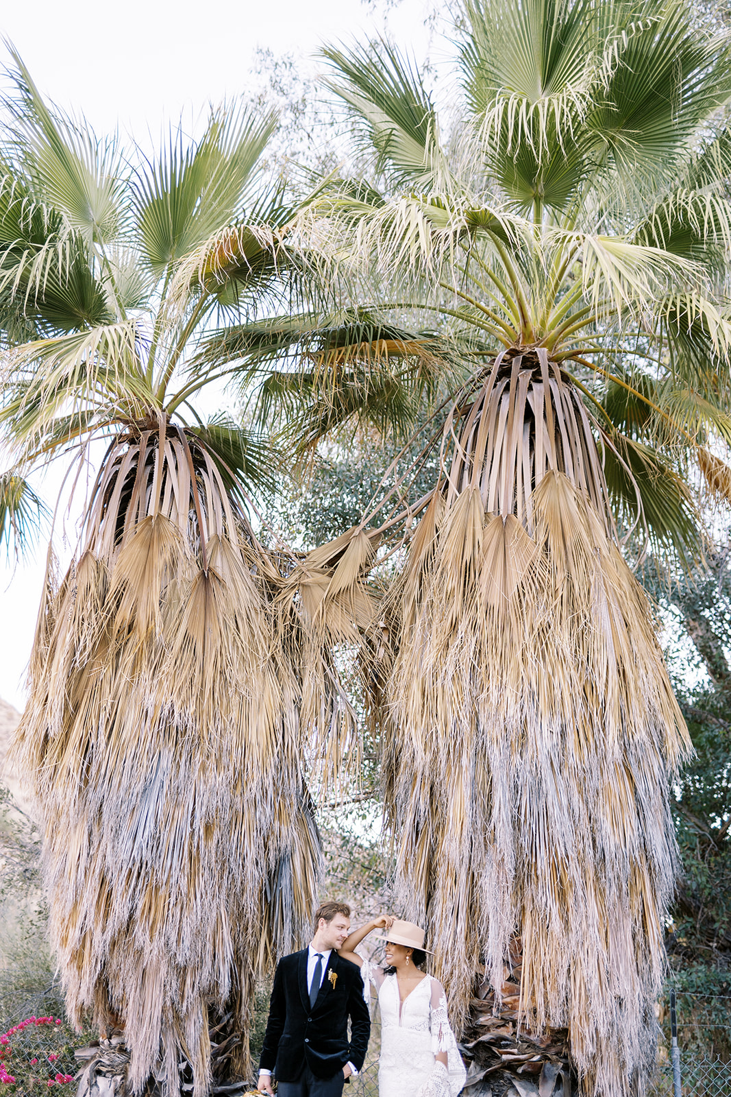Man and woman in front of two giant palm trees for desert elopement photos. 