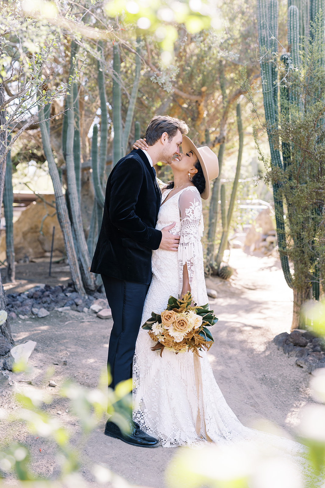 Woman smiling at man while man looks at her while holding her. They are surrounded by desert cactus and are in a private area. Desert elopement planning