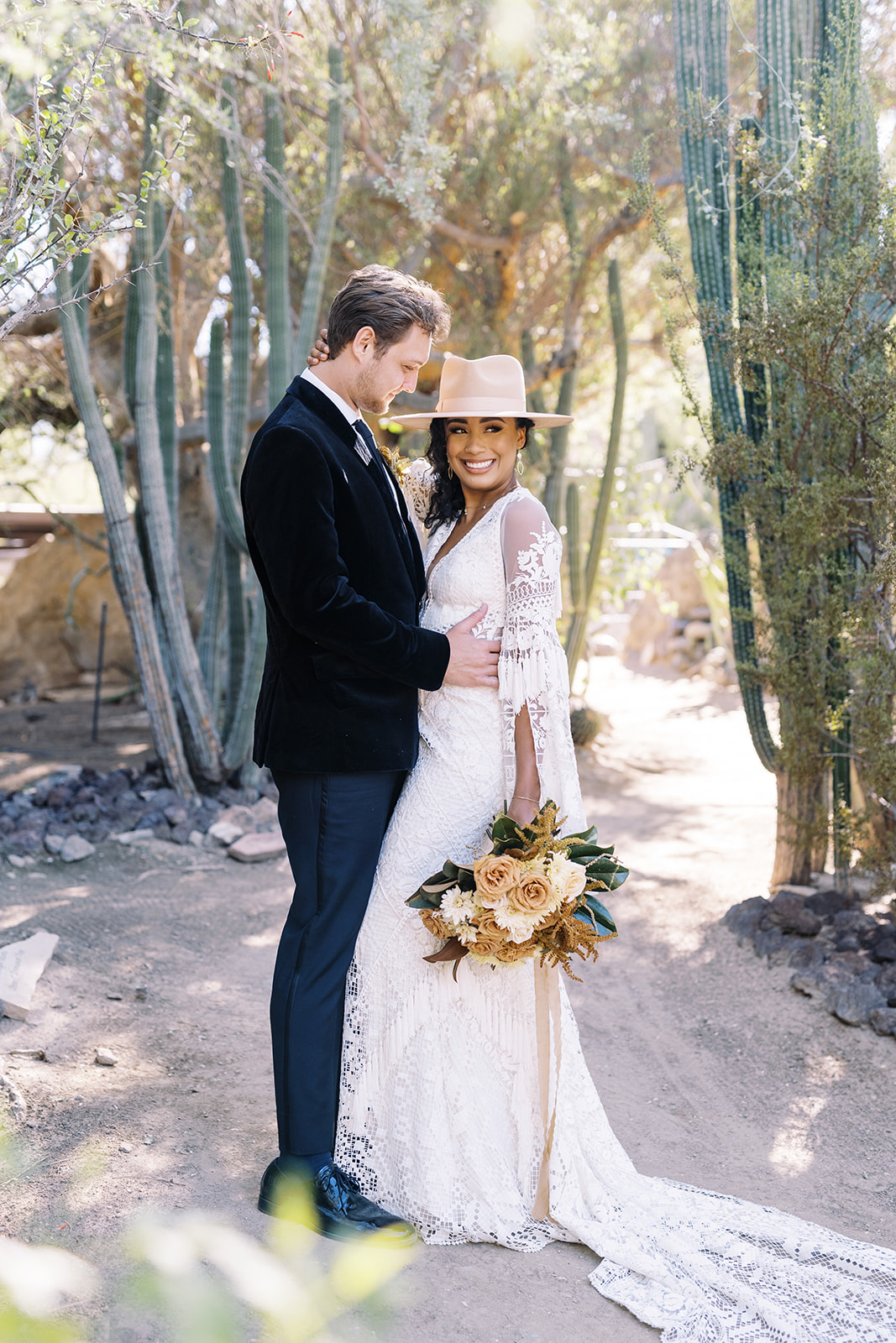 Woman smiling at camera while man looks at her while holding her. They are surrounded by desert cactus and are in a private area. Desert elopement planning