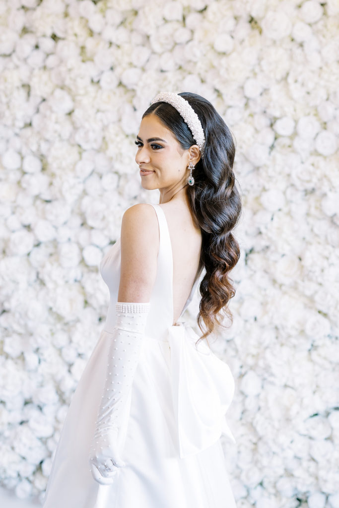 Bride standing in front of wall of white roses in wedding dress. Texas wedding photography
