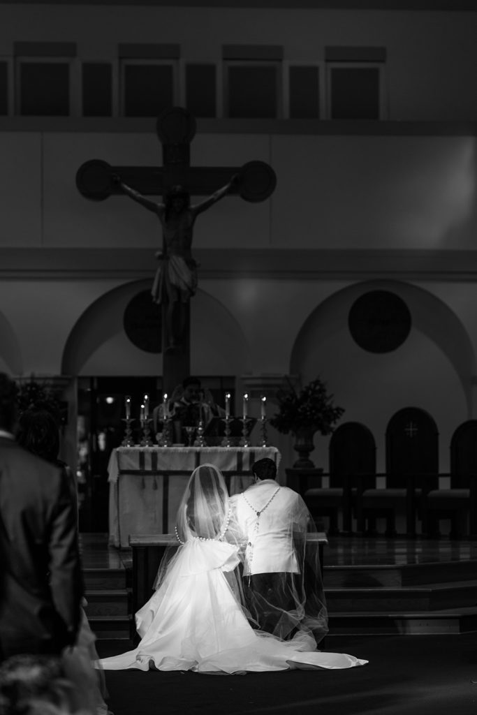 Catholic church ceremony with bride and groom on knees during ceremony. 