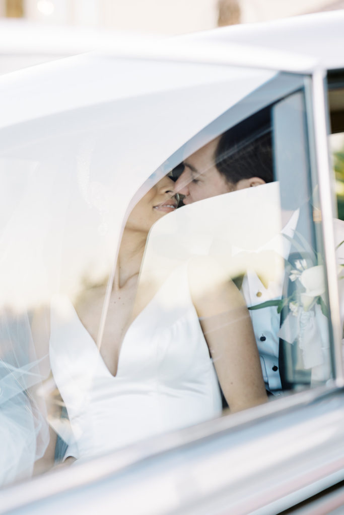 Wedding photo of bride and groom kissing in car with reflection from glass.