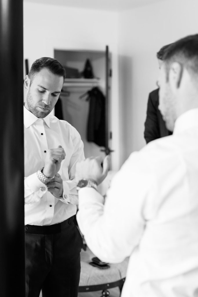 groom getting ready by putting on tuxedo inside groomsmen house at texas wedding venue
