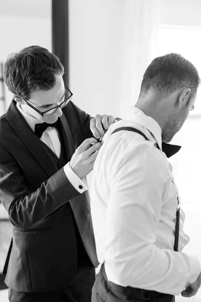 groom getting ready by putting on tuxedo inside groomsmen house at texas wedding venue