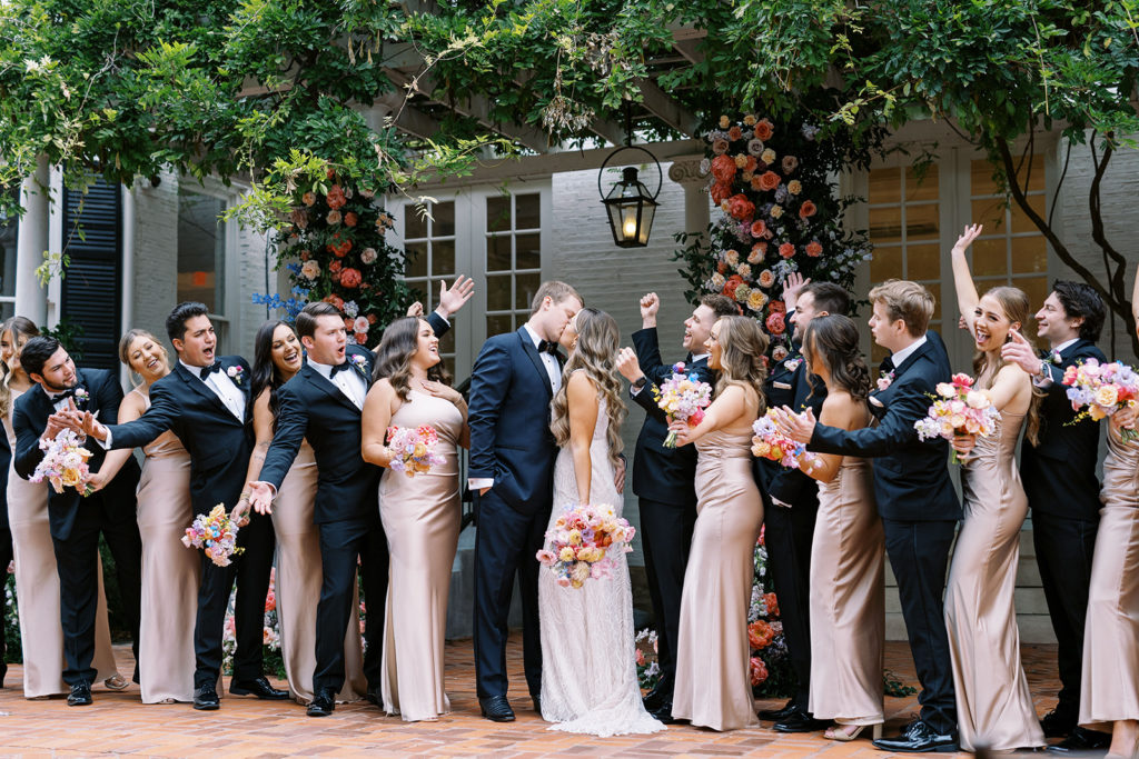 bridal party cheering on bride and groom while bride and groom kiss