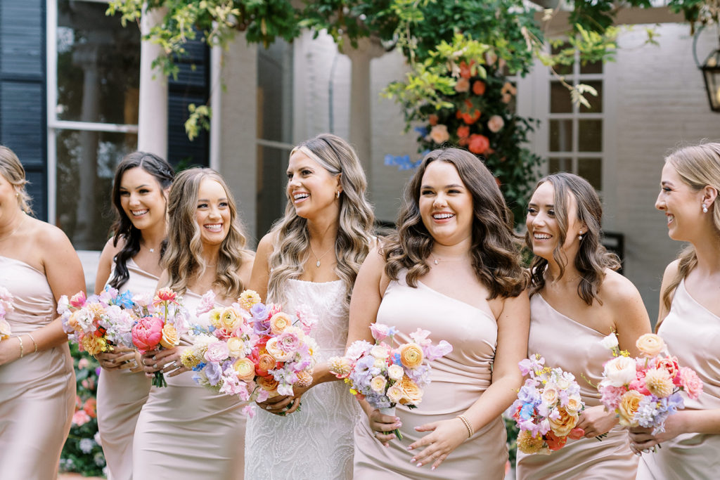 bridesmaids laughing with bride while holding colorful wedding flower bouquets